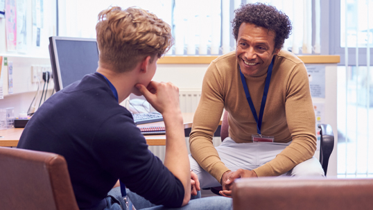 Male College Student Meeting With Campus Counselor Discussing Mental Health Issues