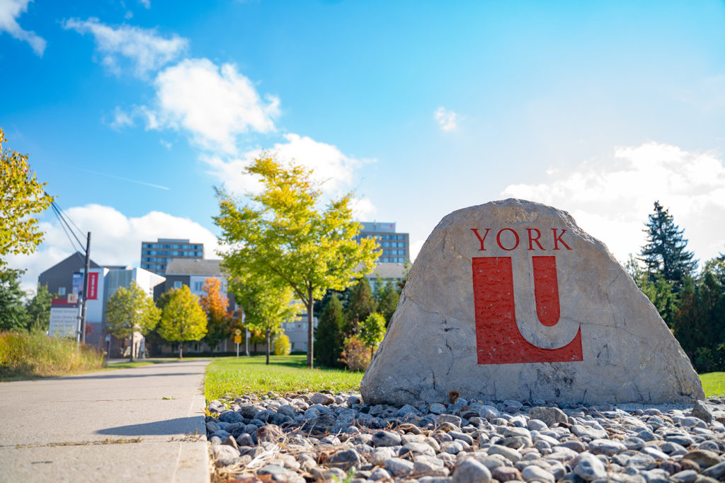 YorkU west entrance large stone with blue sky and autumn coloured trees