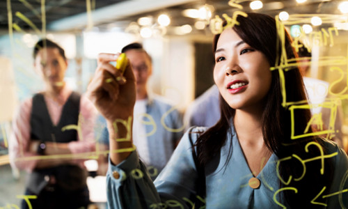 focus on young east asian woman using marker to write on transparent whiteboard