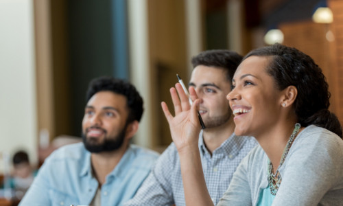 focus on cheerful female student raising her hand to answer question in seminar