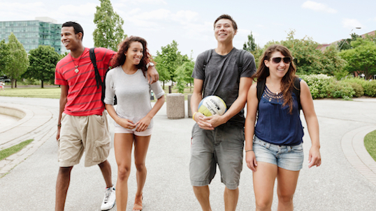Four students, one male with a volleyball, walking on the Keele campus and smiling