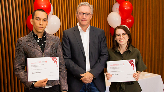 Two students with their Writing Prizes in their hands standing beside a professor