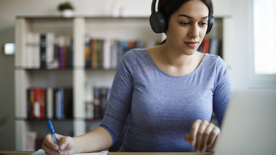 Girl wearing a blue sweater and headphones watching something on her laptop