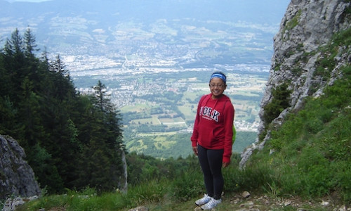 York student in a red York sweater standing on a hillside smiling at the camera