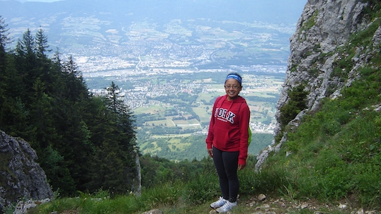 York student in a red York sweater standing on a hillside smiling at the camera