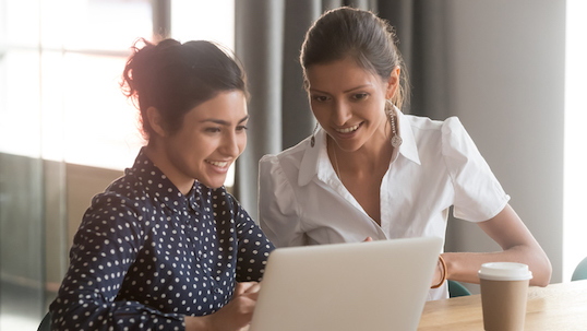 Two women looking at a laptop screen with a cup of coffee on the table