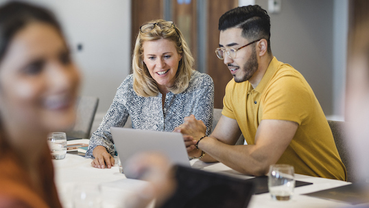 A woman and male student looking at a laptop on the table and smiling