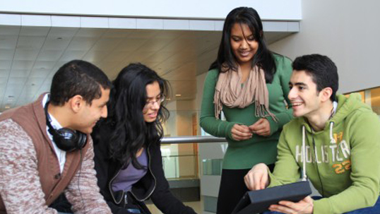 four students discussing schoolwork on tablet device