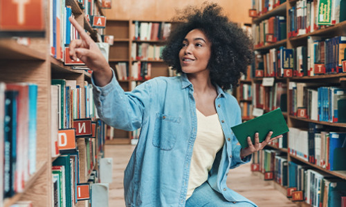 English & Professional Writing black girl sitting on floor of library looking at shelves
