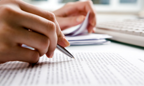 hand holding pen reviewing pages of text