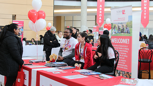 York students talking to passerby during fair in Vari Hall