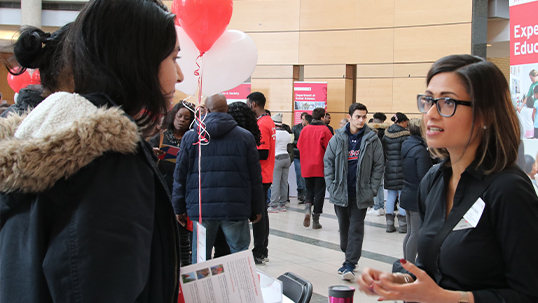 Volunteers speaking to students in vari hall at open house