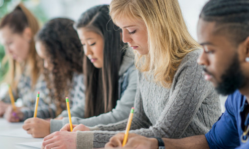 side view of students sitting in a row and writing an exam