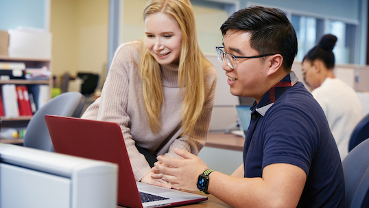 a young woman and a man look at the laptop screen while they smile