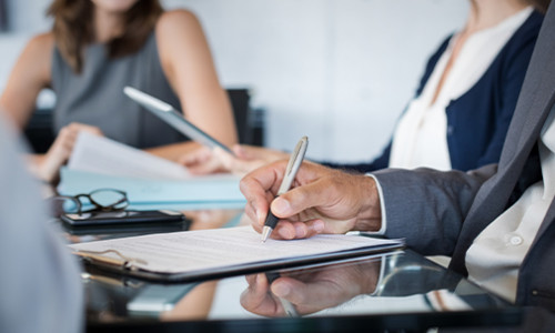 image of a hand holding a pen writing on a document on a clipboard while