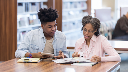 An African American teacher helps her student before class