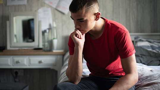 a young man sits on his bed thinking