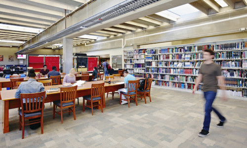 image of a library with students at the tables and a person passing by
