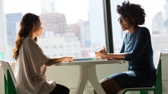 Two women sitting across from each other at a table while having a conversation