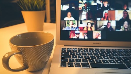 Coffee mug and small plant placed next to Macbook Pro laptop with video conference call on screen