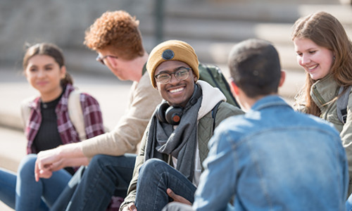 a group of diverse students sitting outdoors on the steps while they smile and talk