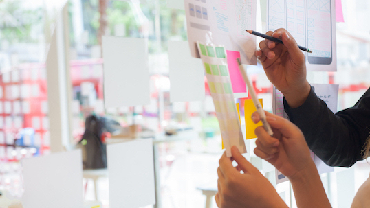 hands writing on sticky notes on a board