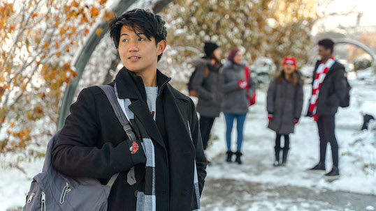 Male student in winter attire looks into the distance with four other students standing in background