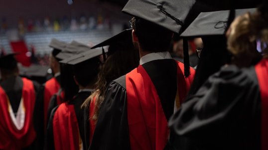 Students in black convocation robes and caps line up during graduation ceremony