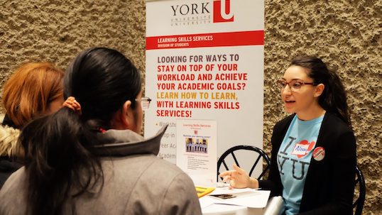 York University workshop volunteer stands next to poster while talking with students