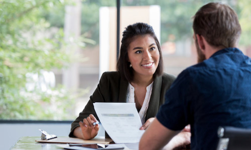 Hispanic businesswoman smiles while showing a document to a male associate