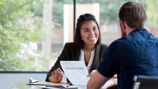 Hispanic businesswoman smiles while showing a document to a male associate