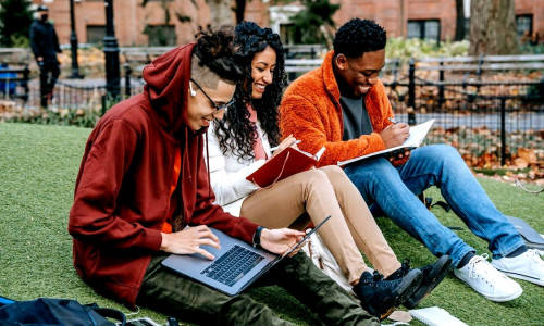 Three students seating on the grass studying