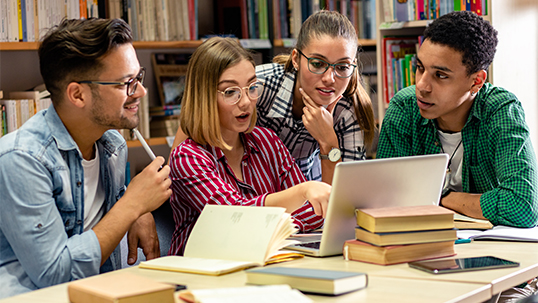 Four young students reading together on a laptop.