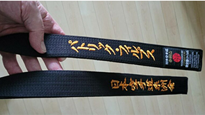 Phillips’s black belt. The inscription reads “Patrick Phillips” in Japanese (displayed top of the belt) with the name of the Japanese Karate Organization (bottom of the belt)