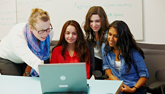 instructor explaining to three female students in front of laptop