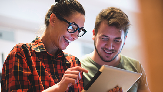 Two people smiling while looking at a tablet