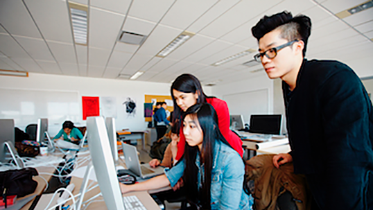 Three students in a computer lab looking onto the computer