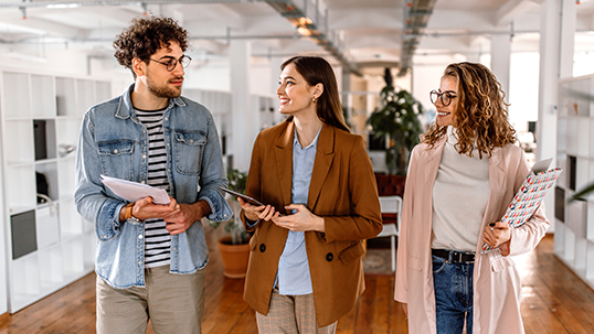 Group of smiling coworkers walking through the office, discussing about work project