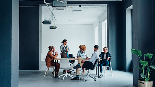 Multi ethnic team of five smiling businessman and businesswoman discussing ideas together during a casual meeting at the office desk.