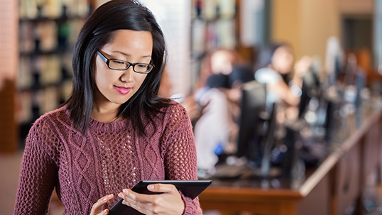 Asian college student or teaching assistant using tablet in library