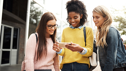 Women, students and friends with phone in social media, communication or streaming outside campus