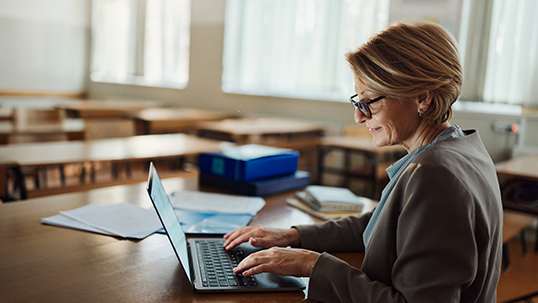 Smiling female teacher working on laptop in the classroom