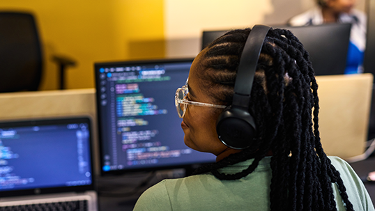 Computer programmer working with headset and multiple screens in office