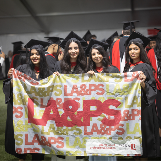Four graduates wearing academic gowns and caps hold an LA&PS banner while posing for a photo at a convocation celebration