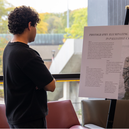 A participant stands reading a research display board during a poster presentation session at an academic showcase