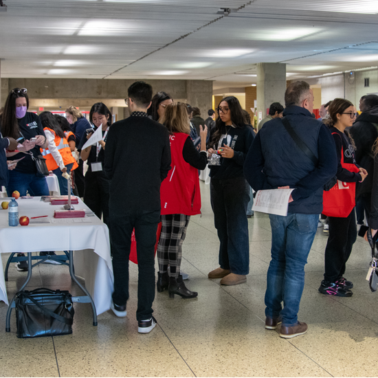 Attendees visit an information table in a campus hallway, where staff members provide brochures and answer questions during a recruitment event.