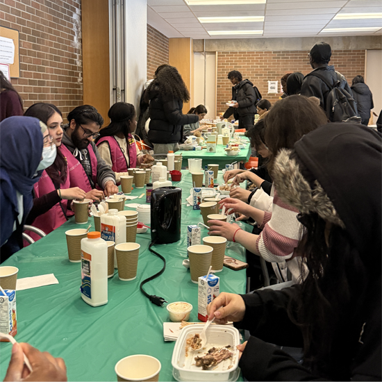 Students and volunteers seated along a long table share a meal and conversation during a First Year Lunch Break gathering
