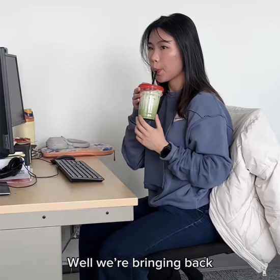 A person seated at a desk beside a computer drinks a green beverage through a straw, with caption text at the bottom reading “Well we’re bringing back.