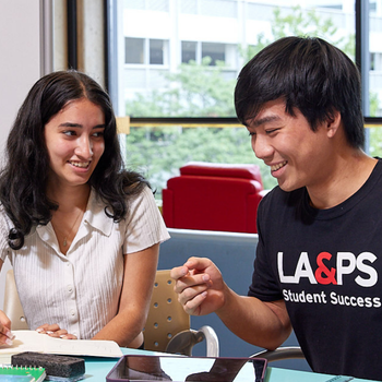 Two students collaborate at a table, reviewing notes during a peer tutoring session