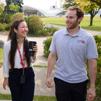 Two people walk and talk together on campus along a landscaped pathway
